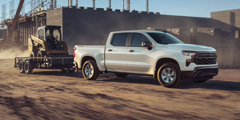 White Chevrolet Silverado 1500 pickup truck towing construction equipment at a building site.